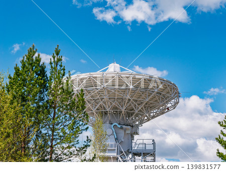 A large telescope antenna with multiple stairs stands tall at a scientific observatory under a bright blue sky A large telescope antenna with multiple stairs stands tall at a scientific observatory under a bright blue sky 139831577