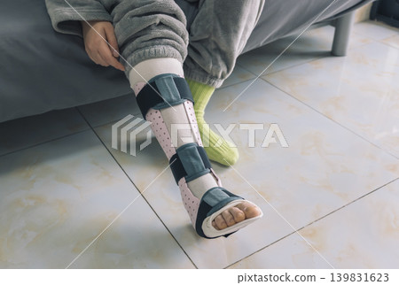 A person sits indoors, their lower leg secured in a pink and black medical splin A person sits indoors, their lower leg secured in a pink and black medical splin 139831623