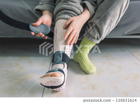 Hands adjust the strap on a patient's light pink perforated medical foot and ankle brace 139831624