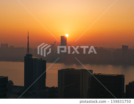 Aerial perspective capturing the sunrise over Hangzhou, China. Silhouetted buildings are visible against the vibrant red and orange sky. City view at dawn with rising sun. Aerial perspective capturing the sunrise over Hangzhou, China. Silhouetted buildings are visible against the vibrant red and orange sky. City view at dawn with rising sun. 139831750