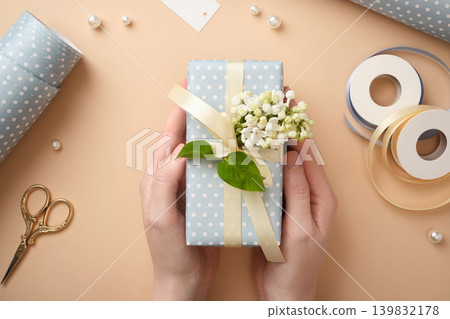 The hands are holding a ready-wrapped gift with a yellow ribbon and a lilac flower. The hands are holding a ready-wrapped gift with a yellow ribbon and a lilac flower. 139832178