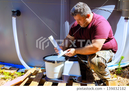 Worker works fixes cleaning pool filter pump water tank near swimming pool on sunny day. Worker works fixes cleaning pool filter pump water tank near swimming pool on sunny day. 139832182