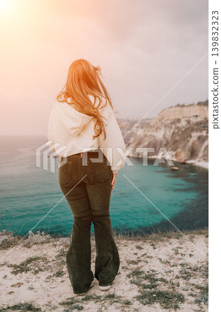 Woman sea cliff Young woman standing on a cliff edge looking at the turquoise ocean and rocky coastline during sunset Woman sea cliff Young woman standing on a cliff edge looking at the turquoise ocean and rocky coastline during sunset 139832323
