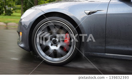 Wheel of modern electrical automobile driving at urban road on rainy day. Ecology friendly car riding moving along motorway. Electric vehicle riding through empty highway. Green innovation concept Wheel of modern electrical automobile driving at urban road on rainy day. Ecology friendly car riding moving along motorway. Electric vehicle riding through empty highway. Green innovation concept 139832393