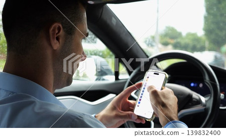 Male entrepreneur browsing modern smartphone while riding autonomous self driving electric car at city. Successful businessman using phone during riding on electrical auto with autopilot at rainy day 139832400