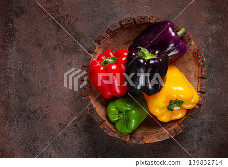 A collection of colorful bell peppers, in a wooden bowl, on a dark surface, top view, no people A collection of colorful bell peppers, in a wooden bowl, on a dark surface, top view, no people 139832714