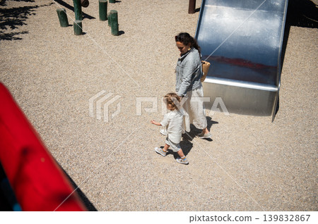 Mother and son walking by a slide at a sunny playground enjoying time together Mother and son walking by a slide at a sunny playground enjoying time together 139832867