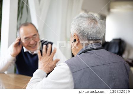 A senior Japanese man wearing a hearing aid while conversing. 139832939