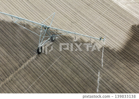 Agricultural irrigation sprinkler watering dry soil on farm field for crops growing during period of drought Agricultural irrigation sprinkler watering dry soil on farm field for crops growing during period of drought 139833138