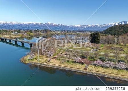 空拍照片顯示岩手縣禦所湖周圍的櫻花樹和白雪皚皚的山峰。 空拍照片顯示岩手縣禦所湖周圍的櫻花樹和白雪皚皚的山峰。 139833256