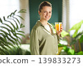 Cheerful Woman Holding Orange Juice in Sunlit Home 139833273