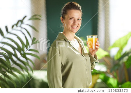 Cheerful Woman Holding Orange Juice in Sunlit Home Cheerful Woman Holding Orange Juice in Sunlit Home 139833273