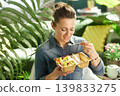 Smiling Woman Holding a Piece of Fruit on a Wooden Fork 139833275