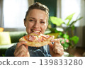 Smiling Woman Holding Pizza in a Cozy Living Room 139833280