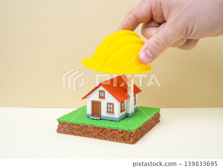 A yellow construction helmet is placed on the house. Building renovation or reconstruction, housing modernization and improvement of residential infrastructure. A yellow construction helmet is placed on the house. Building renovation or reconstruction, housing modernization and improvement of residential infrastructure. 139833695