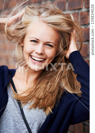 Portrait, happy and woman with wind in hair by brick wall in city, funny or laugh outdoor. Face, fashion and smile of person, stylish casual clothes and blonde girl with breeze in Switzerland Portrait, happy and woman with wind in hair by brick wall in city, funny or laugh outdoor. Face, fashion and smile of person, stylish casual clothes and blonde girl with breeze in Switzerland 139834026