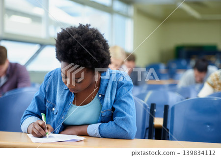 Writing, university and black woman student in classroom studying for test, exam or assignment. Education, college and female person working on project with knowledge in lecture hall for learning. Writing, university and black woman student in classroom studying for test, exam or assignment. Education, college and female person working on project with knowledge in lecture hall for learning. 139834112