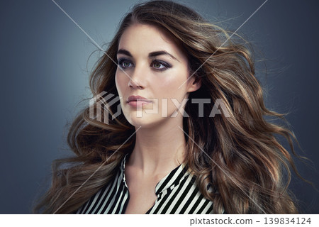 Woman, beauty and hair in studio with cosmetics, thinking of makeup and smokey eye aesthetic. Young and serious model or person with trendy style, treatment and blowing in wind on grey background Woman, beauty and hair in studio with cosmetics, thinking of makeup and smokey eye aesthetic. Young and serious model or person with trendy style, treatment and blowing in wind on grey background 139834124