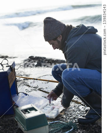 Cold, gear and beach with fisherman, cooler box and hobby with equipment and weekend break. Person, ocean and guy with tools for activity and early morning with waves, shore and seaside with vacation Cold, gear and beach with fisherman, cooler box and hobby with equipment and weekend break. Person, ocean and guy with tools for activity and early morning with waves, shore and seaside with vacation 139834143