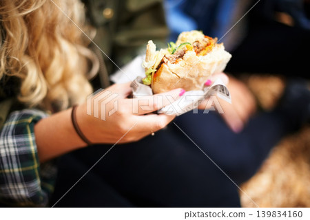 Woman, hands and burger with hungry for food, nutrition and take away on holiday in outdoor. Person, eating and satisfaction with protein roll in hand, closeup or foodie outside on vacation leisure Woman, hands and burger with hungry for food, nutrition and take away on holiday in outdoor. Person, eating and satisfaction with protein roll in hand, closeup or foodie outside on vacation leisure 139834160