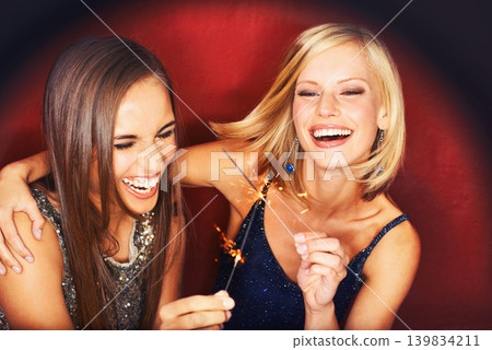 Friends, celebration and women with sparklers, excited and laughing for night event in studio. Fireworks, happiness and couple of girls together on red background for party, gathering and energy. Friends, celebration and women with sparklers, excited and laughing for night event in studio. Fireworks, happiness and couple of girls together on red background for party, gathering and energy. 139834211