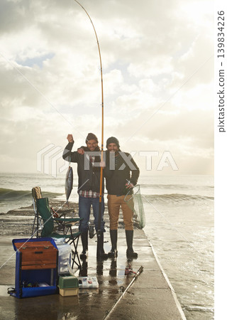 Happy, portrait and people at ocean fishing with pride to catch tuna on pier at sunset. Fisherman, friends and smile holding fish in hand on adventure in nature at sea for holiday or vacation 139834226