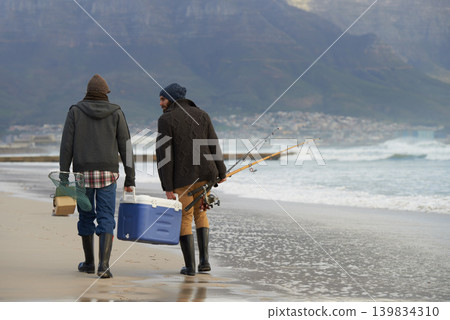 Ocean, fishing and men walking together with cooler, tackle box and holiday conversation from back. Beach, fisherman and friends with rods, bait and tools at waves on winter morning vacation at sea. Ocean, fishing and men walking together with cooler, tackle box and holiday conversation from back. Beach, fisherman and friends with rods, bait and tools at waves on winter morning vacation at sea. 139834310