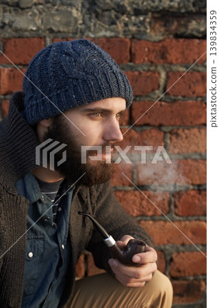 Face, winter and pipe smoke with man outdoor on wall background for fashion, style or clothing. Morning, tobacco or habit and young person with beanie smoking in cold weather season to relax Face, winter and pipe smoke with man outdoor on wall background for fashion, style or clothing. Morning, tobacco or habit and young person with beanie smoking in cold weather season to relax 139834359