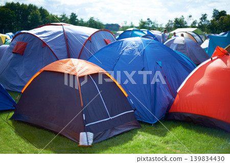 Group, colourful and camping tents in nature outside of a music festival campsite. Row of canopies placed on ground at musical concert, entertainment event and carnival celebration outdoor on grass 139834430