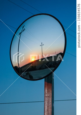 Vertical shot of a Spectacular sunset reflected in a circular mirror placed on a telephone pole on the Spanish island of Menorca. 139834576