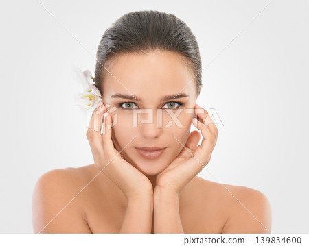 Woman, portrait and orchid with glow for skincare in studio, beauty and natural makeup for blossom. Girl, plant and white background, closeup and hands on face with cosmetics dermatology for wellness Woman, portrait and orchid with glow for skincare in studio, beauty and natural makeup for blossom. Girl, plant and white background, closeup and hands on face with cosmetics dermatology for wellness 139834600