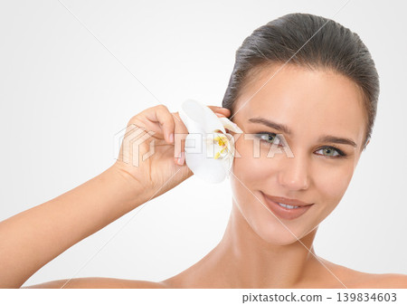 Woman, face and flower with glow for skincare in studio, beauty and natural makeup for blossom. Girl, orchid and hair with background, portrait and closeup with cosmetics dermatology for wellness Woman, face and flower with glow for skincare in studio, beauty and natural makeup for blossom. Girl, orchid and hair with background, portrait and closeup with cosmetics dermatology for wellness 139834603