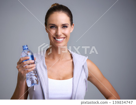 Fitness, portrait and happy woman with water in studio for training, wellness or detox on grey background. Sports, bottle and face of female model with liquid hydration for body workout recovery Fitness, portrait and happy woman with water in studio for training, wellness or detox on grey background. Sports, bottle and face of female model with liquid hydration for body workout recovery 139834747