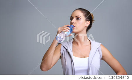 Woman, fitness and drinking water for hydration or natural sustainability on a gray studio background. Face of thirsty female person or athlete with mineral drink in rest, break or recovery on mockup 139834840