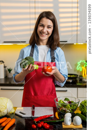 Young woman choosing tomato and broccoli in home kitchen for healthy diet meal prep and nutrition. 139834899