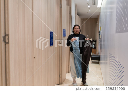 woman holding clothes in fitting room hallway 139834900