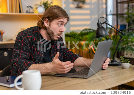 Young man on home table staring at laptop screen in shock and moving closer after major online news 139834916