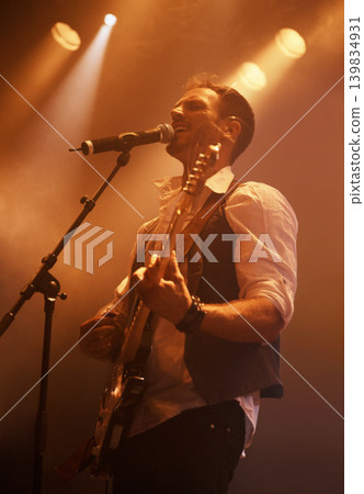 Concert, singer and guitar with man on stage for music, performance and rock show. Event, spotlight and energy with male musician playing instrument at festival club for rave, disco and celebration 139834931