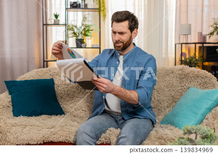 Young man nervously flips through papers and bills, searching for something important at home 139834969