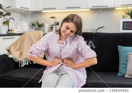 Young woman presses hands to stomach with cramps after heavy food or menstrual pain and seeks relief Young woman presses hands to stomach with cramps after heavy food or menstrual pain and seeks relief 139834981