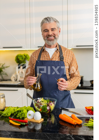 Middle-aged man preparing fresh salad with olive oil in kitchen at home for healthy diet lifestyle Middle-aged man preparing fresh salad with olive oil in kitchen at home for healthy diet lifestyle 139834985