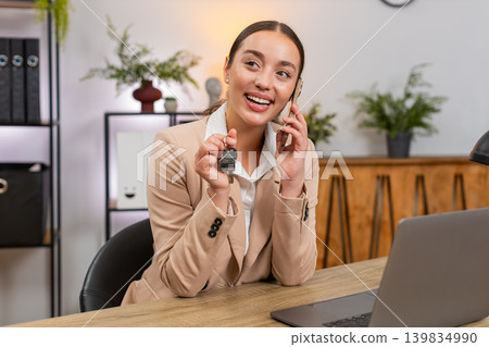 Young businesswoman holds keys to new rented apartment smiles and talks on smartphone with realtor Young businesswoman holds keys to new rented apartment smiles and talks on smartphone with realtor 139834990