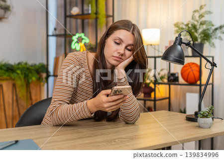 Young woman scrolls smartphone news feed bored unhappy drained by dull repetitive social media posts Young woman scrolls smartphone news feed bored unhappy drained by dull repetitive social media posts 139834996