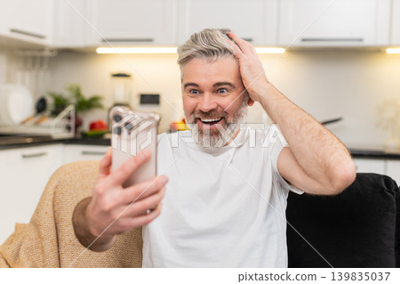 Middle-aged man celebrates good news on smartphone laughs with joy after online game big win success Middle-aged man celebrates good news on smartphone laughs with joy after online game big win success 139835037