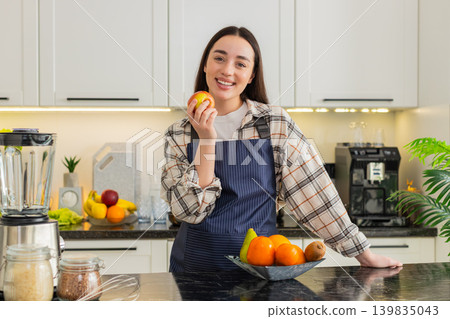 Young woman eating apple in kitchen taking healthy snack break during cooking at home apartment calm Young woman eating apple in kitchen taking healthy snack break during cooking at home apartment calm 139835043