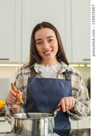 Young woman stirring hot vegetable soup in kitchen pot preparing healthy homemade lunch meal at home Young woman stirring hot vegetable soup in kitchen pot preparing healthy homemade lunch meal at home 139835067