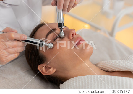 Beautician doctor makes woman micro currents face therapy using electrical impulses in spa salon Beautician doctor makes woman micro currents face therapy using electrical impulses in spa salon 139835127