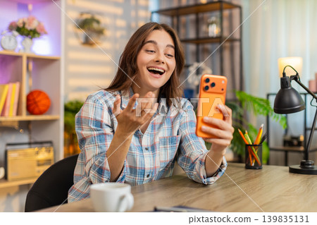 Young woman on home table having video call on smartphone waving during online chat indoors smiling Young woman on home table having video call on smartphone waving during online chat indoors smiling 139835131