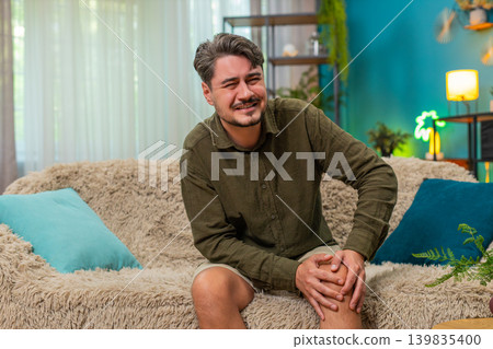 Middle-aged man holding painful knee grimaces bad discomfort arthritis strain seeking relief support 139835400