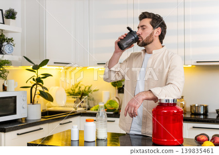 Middle-aged man enjoying protein shake in home kitchen after workout for fitness diet nutrition plan Middle-aged man enjoying protein shake in home kitchen after workout for fitness diet nutrition plan 139835461
